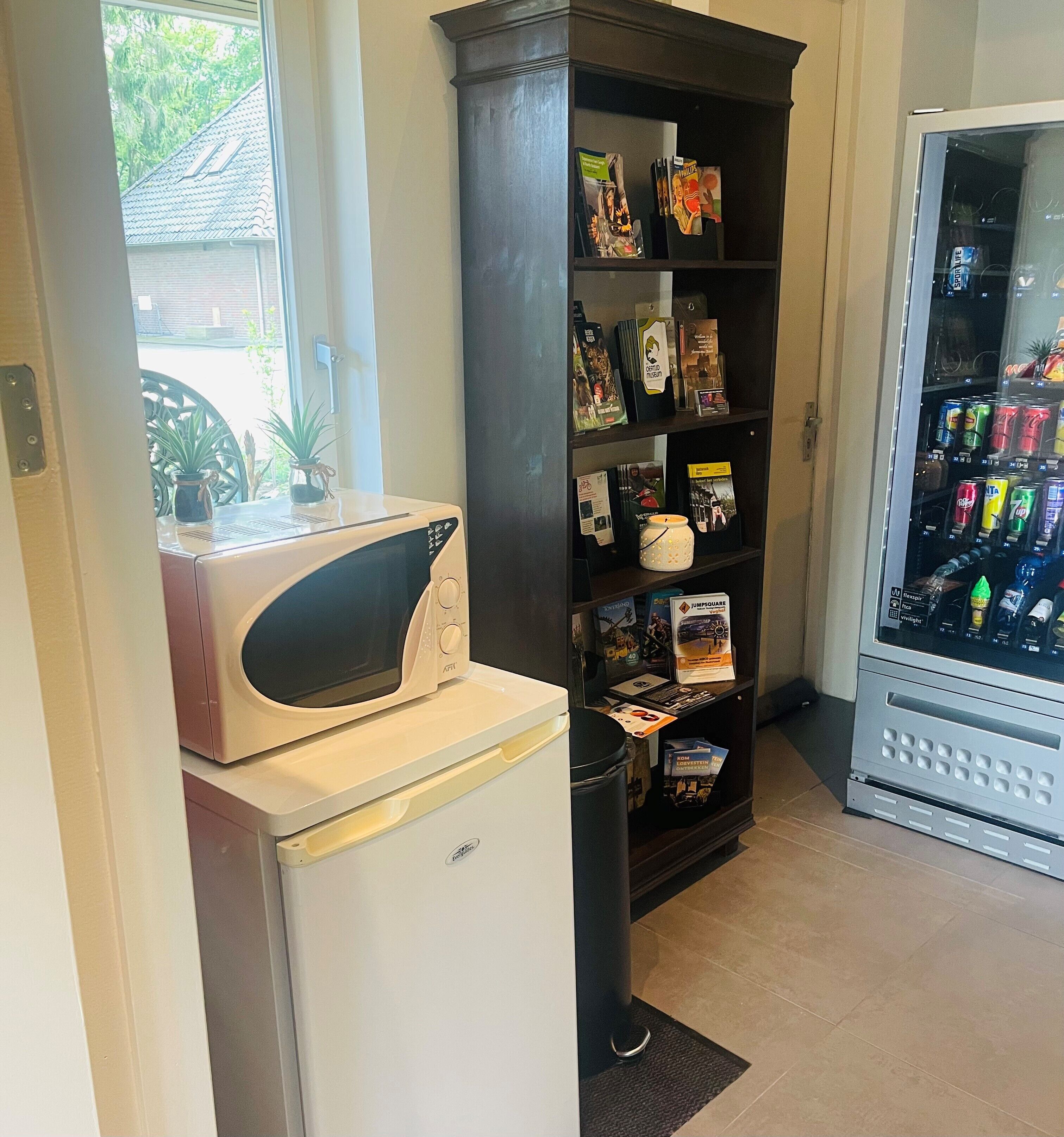A kitchenette with a microwave, a refrigerator, a bookshelf, and a vending machine.