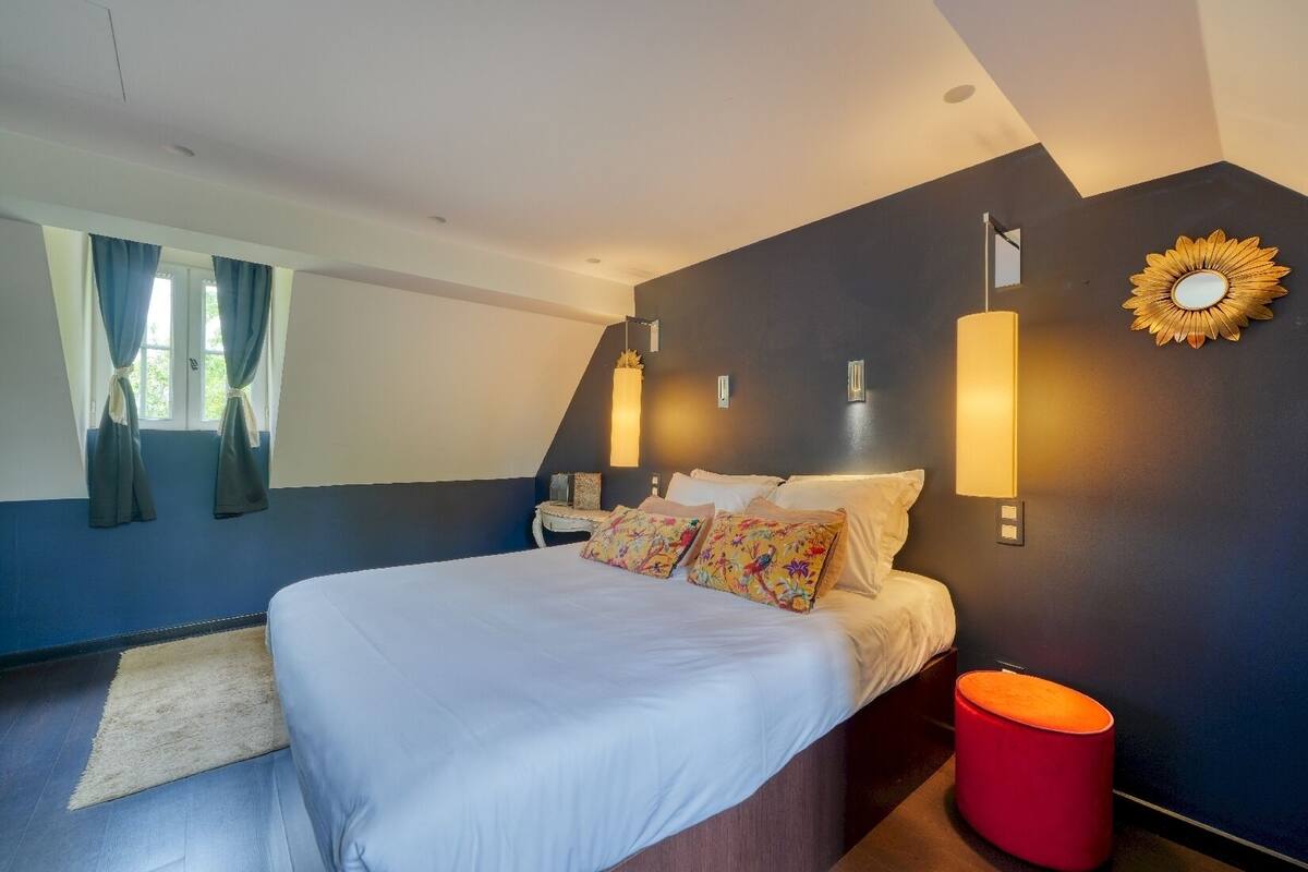 A modern bedroom with a large bed, a red ottoman, and decorative wall sconces.