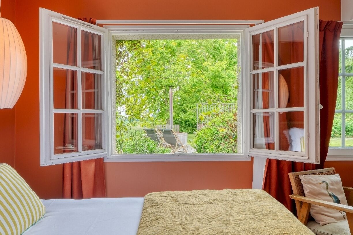 A bedroom with an open window, a bed, and a view of greenery outside.