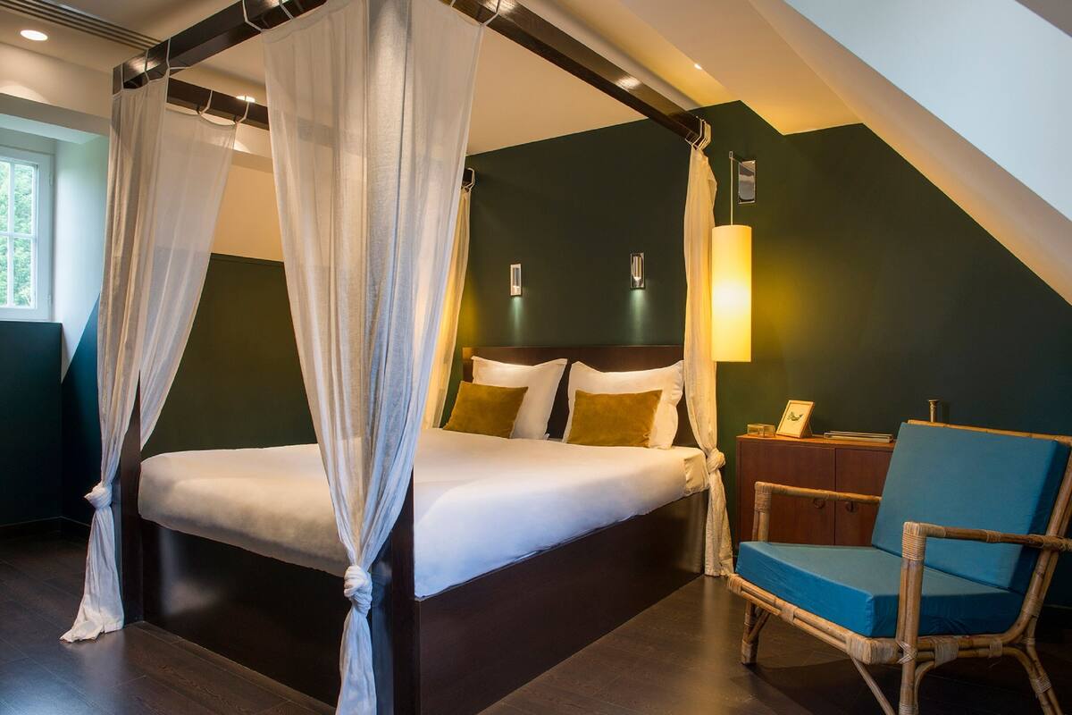 A bedroom with a four-poster bed, a nightstand, a chair, and a lamp.