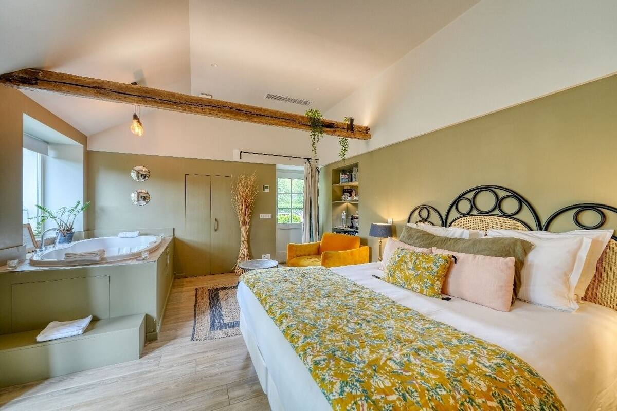 A bedroom with a large bed, a built-in bathtub, and a wooden ceiling beam.