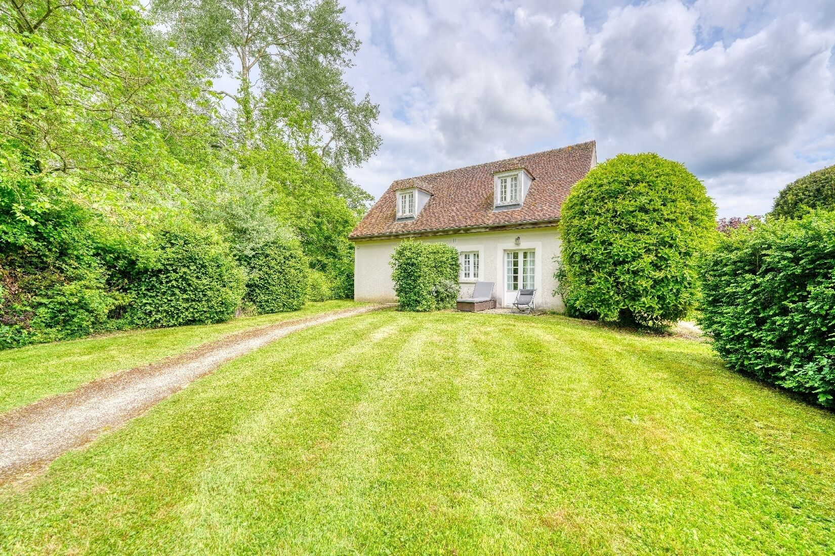 A house with a paved driveway, a lawn, and a small patio area with a chair.