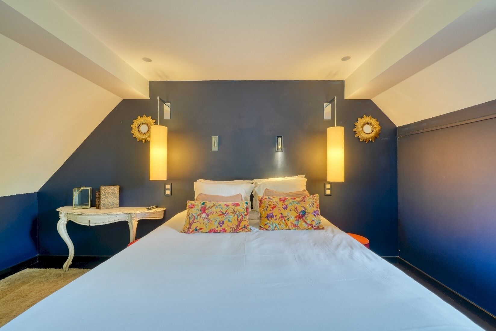 Un dormitorio con una cama grande, dos lámparas fijadas a la pared y una mesita con un objeto decorativo.