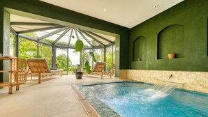 Un área de spa con hidromasaje, sillones de descanso y un patio acristalado con vistas a la vegetación.