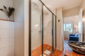 Un baño moderno con cabina de ducha acristalada, suelo de madera y un sofá azul en la sala de estar contigua.