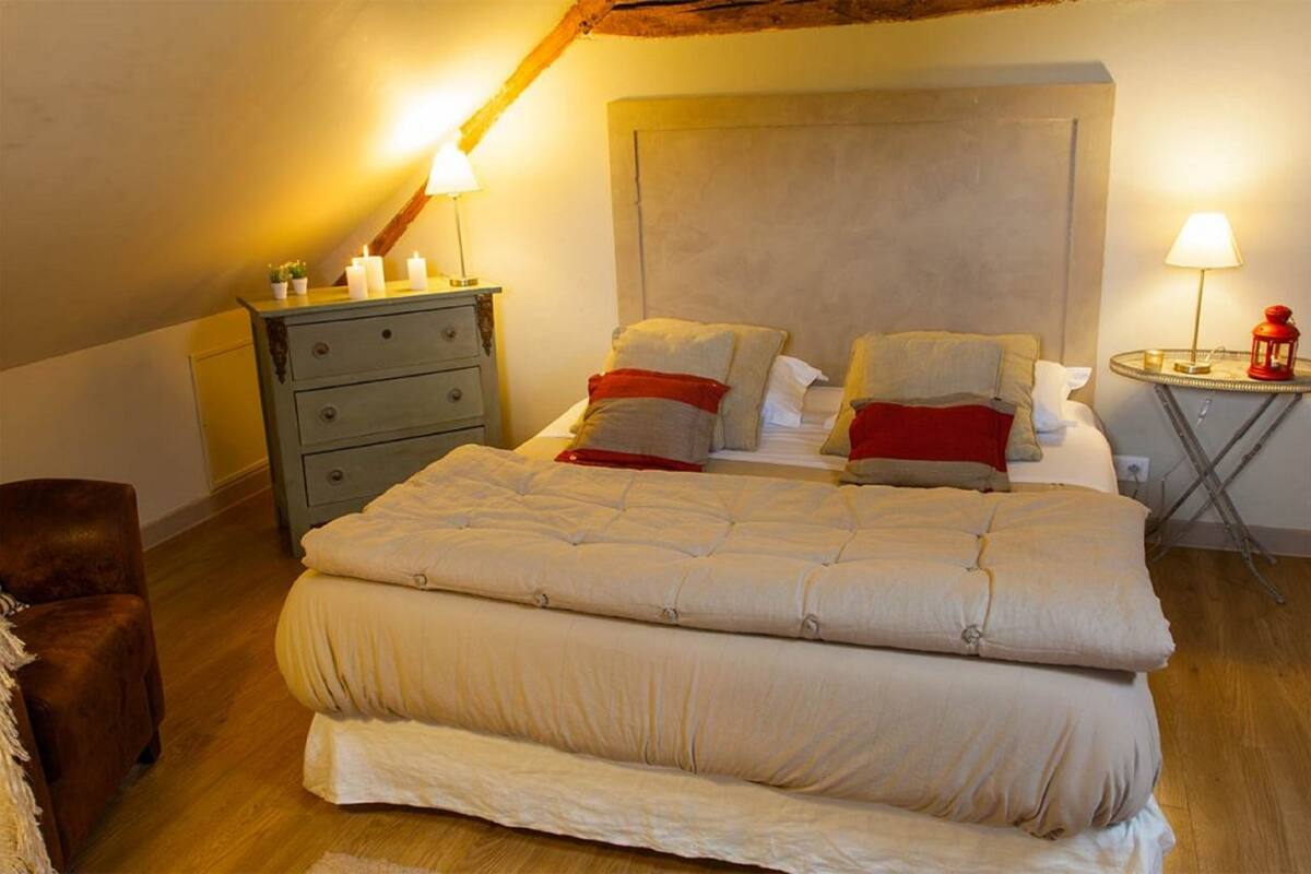 A bedroom with a large bed, a dresser, a chair, and a small table with a lamp.