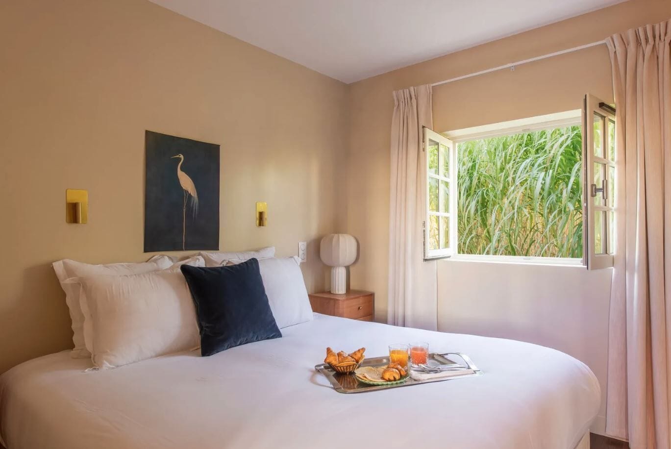 Une chambre d’hôtel avec un lit, un tableau représentant un oiseau, une fenêtre avec des rideaux et un plateau contenant des articles pour le petit-déjeuner.