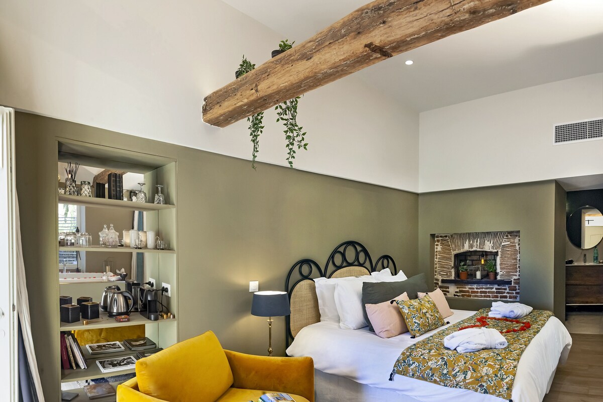 A modern bedroom with a bed, a yellow armchair, a bookshelf, and a fireplace.