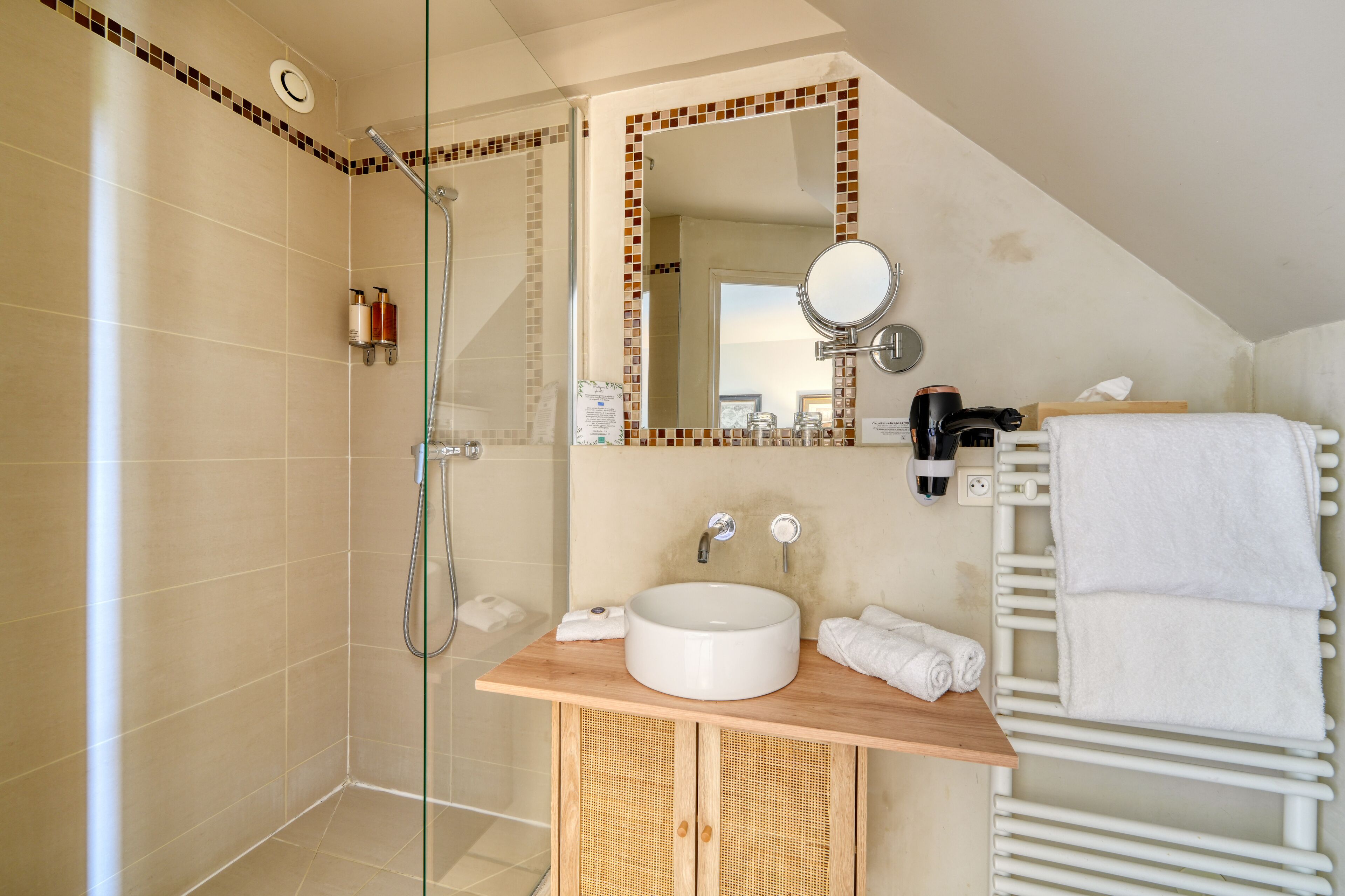 A bathroom with a glass shower enclosure, a wooden vanity with a sink, a mirror, and a towel rack.
