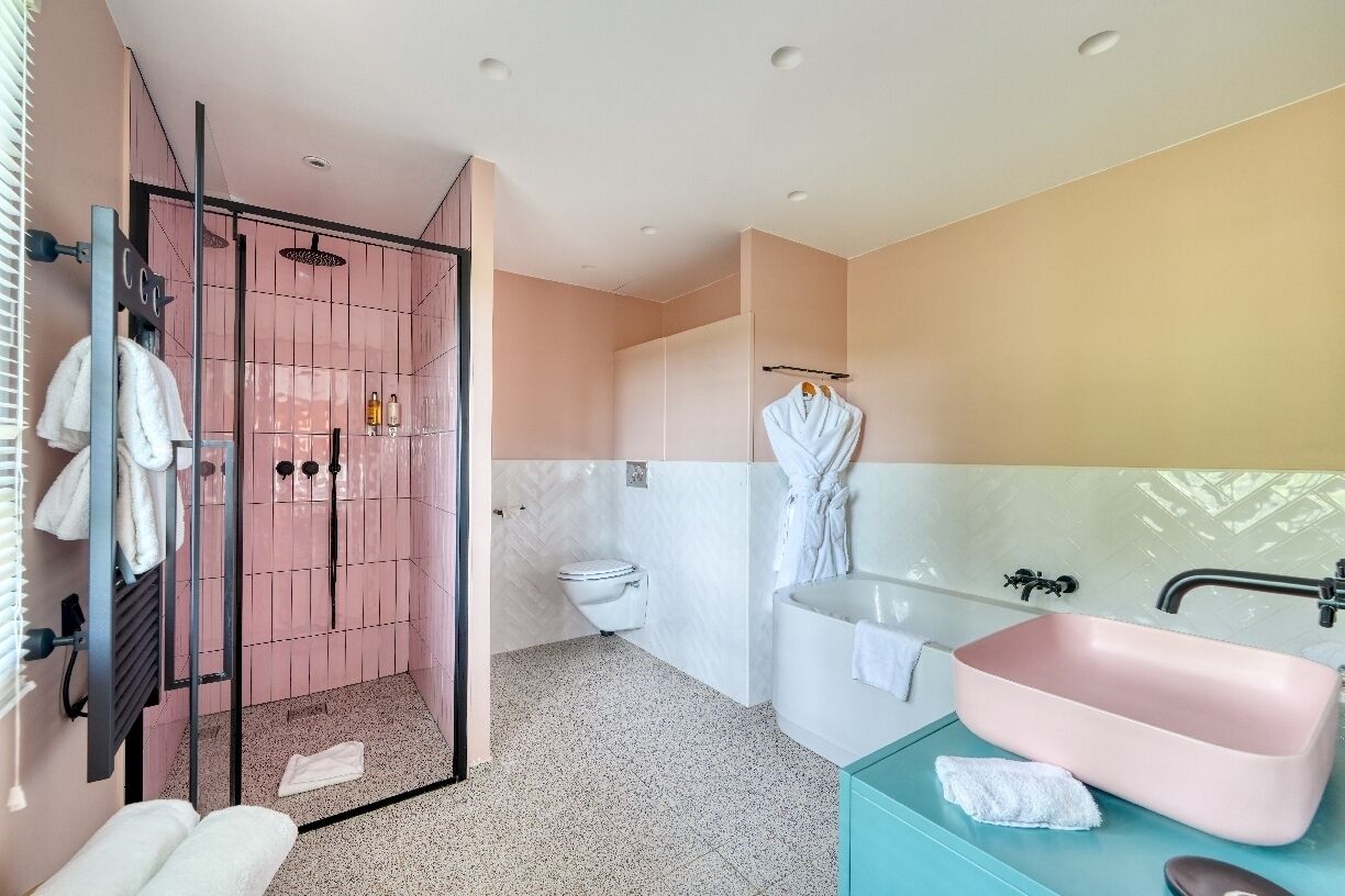 A modern bathroom with a glass-enclosed shower, a white toilet, a pink sink, and a teal vanity.