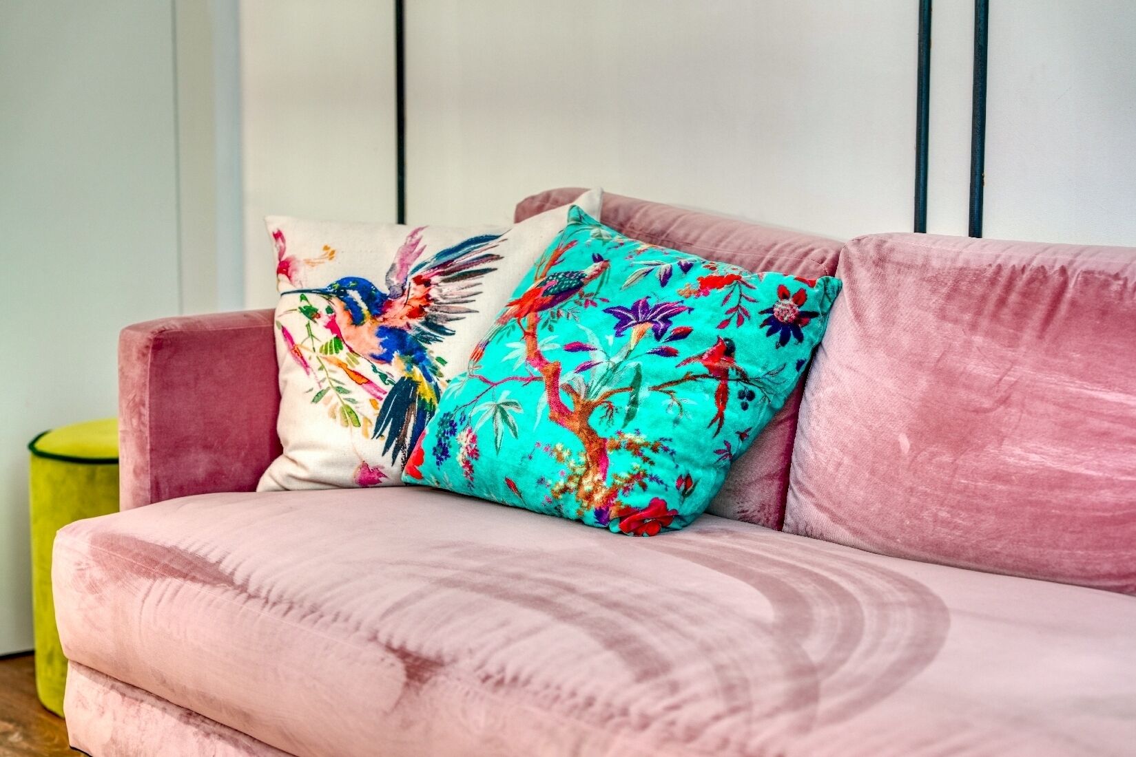 Un sofá rosa con dos almohadones decorativos, uno con estampado floral y el otro con diseño tropical.