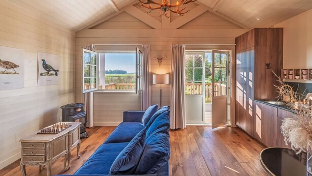 Una habitación acogedora con un sofá azul, suelo de madera, una lámpara de araña y vistas al exterior.