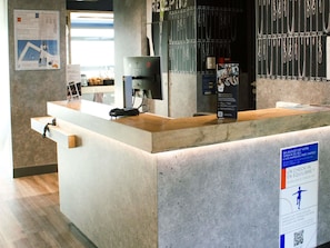 A reception desk with a computer, a phone, and a poster. - ibis budget Saint-Omer Centre (Saint-Omer)
