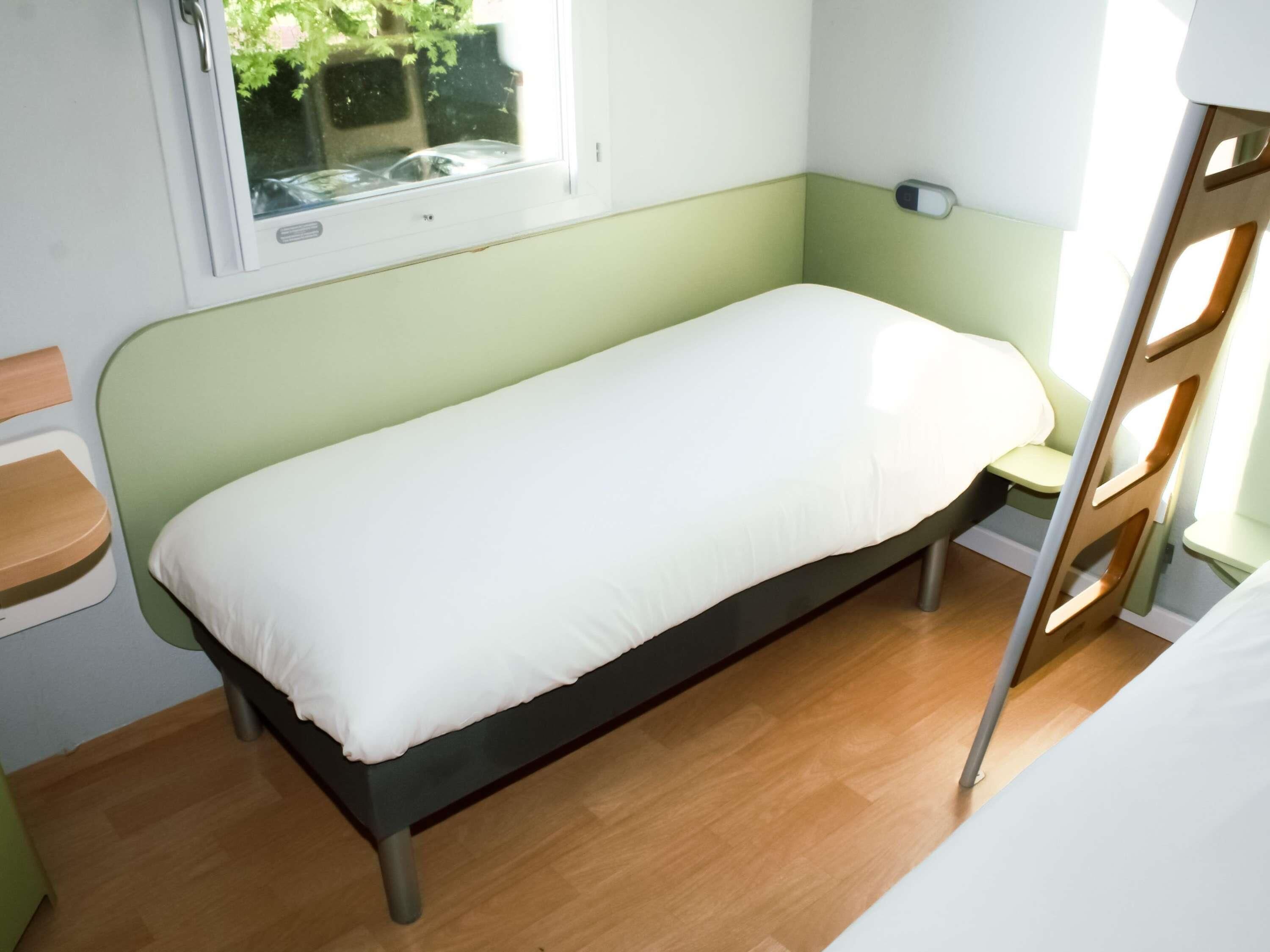 A single bed with a white mattress in a room with green walls and a window.