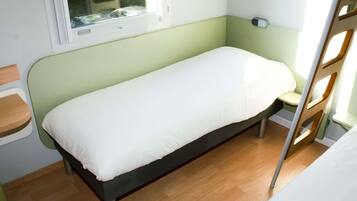 A single bed with a white mattress in a room with green walls and a window.