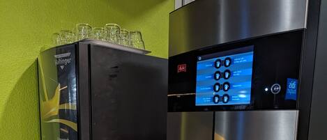 Una cafetera con pantalla digital, una prensa francesa y una bandeja de vasos desechables.