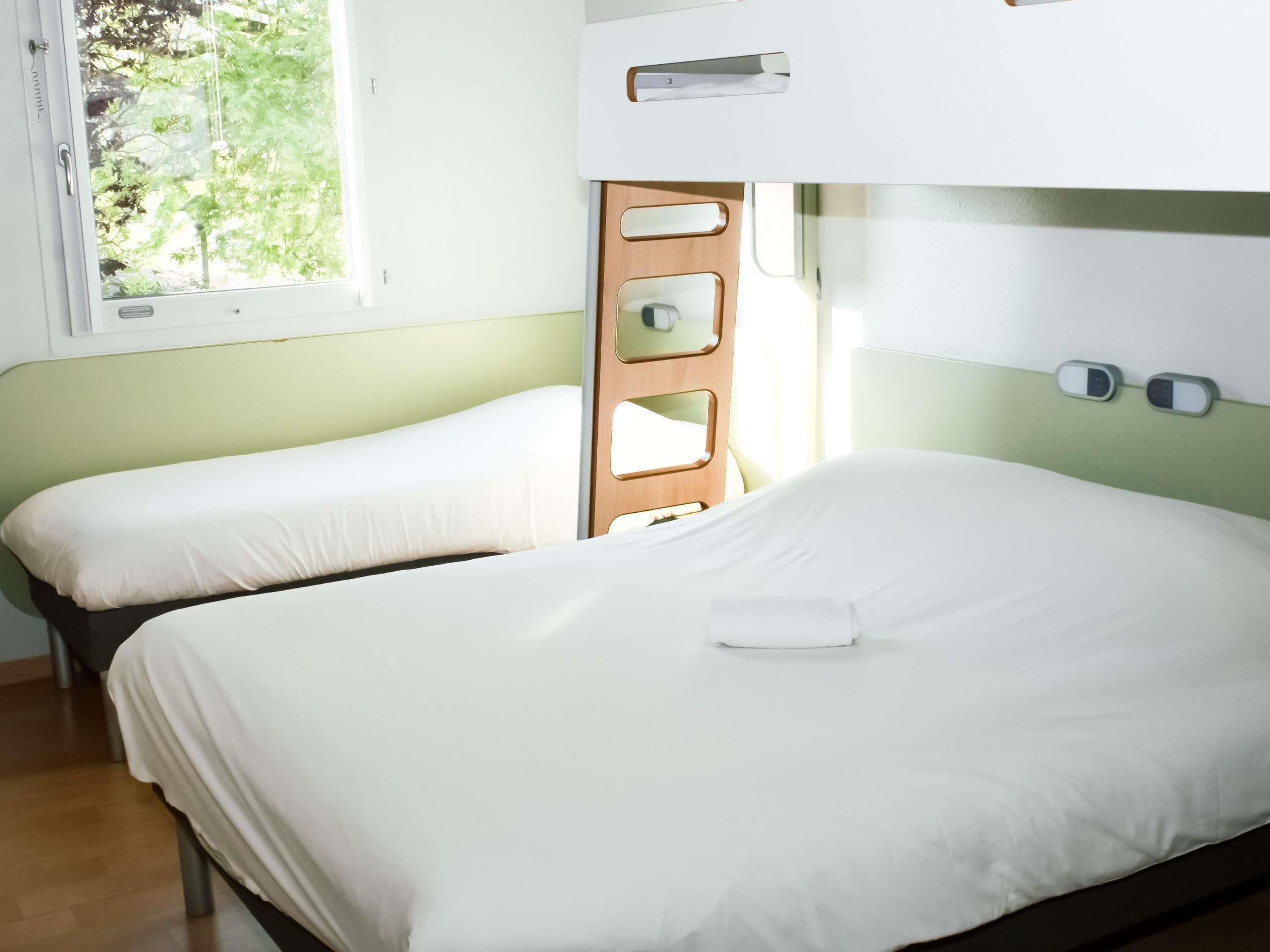 A room with bunk beds, a window with a view of trees, and a bedside table with a lamp.