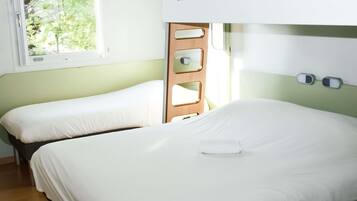 A room with bunk beds, a window with a view of trees, and a bedside table with a lamp.