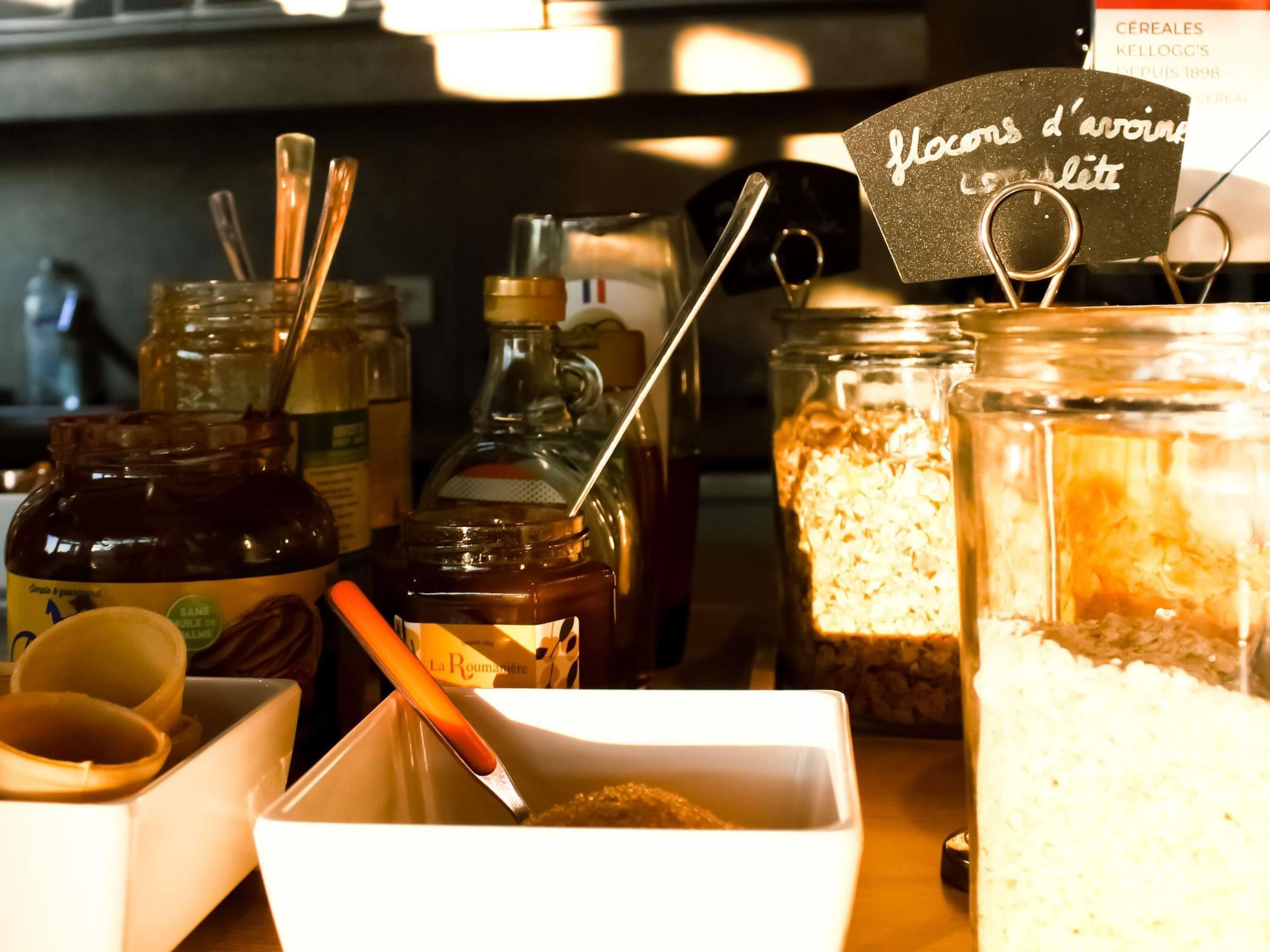A kitchen counter with various food items and containers, including jars and a bowl with a spoon.