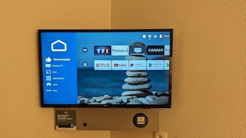 Un televisor montado en la pared muestra una interfaz de servicio de transmisión con varios canales y aplicaciones.