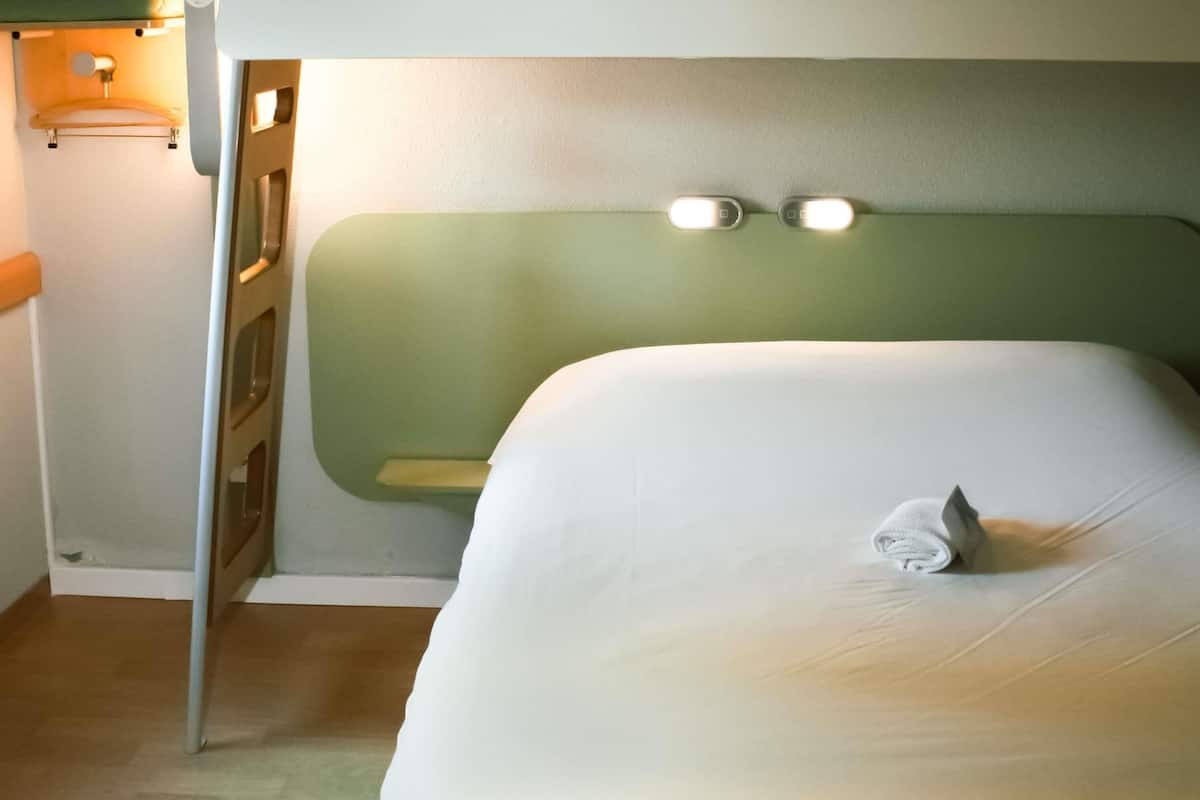 Ein Einzelbett mit dunkelgrünem Kopfteil, einer kleinen Ablagefläche und einem Handtuch auf dem Bett.