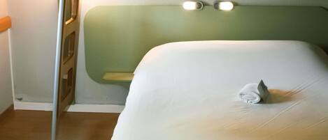 A single bed with a green headboard, a small shelf, and a towel on the bed.