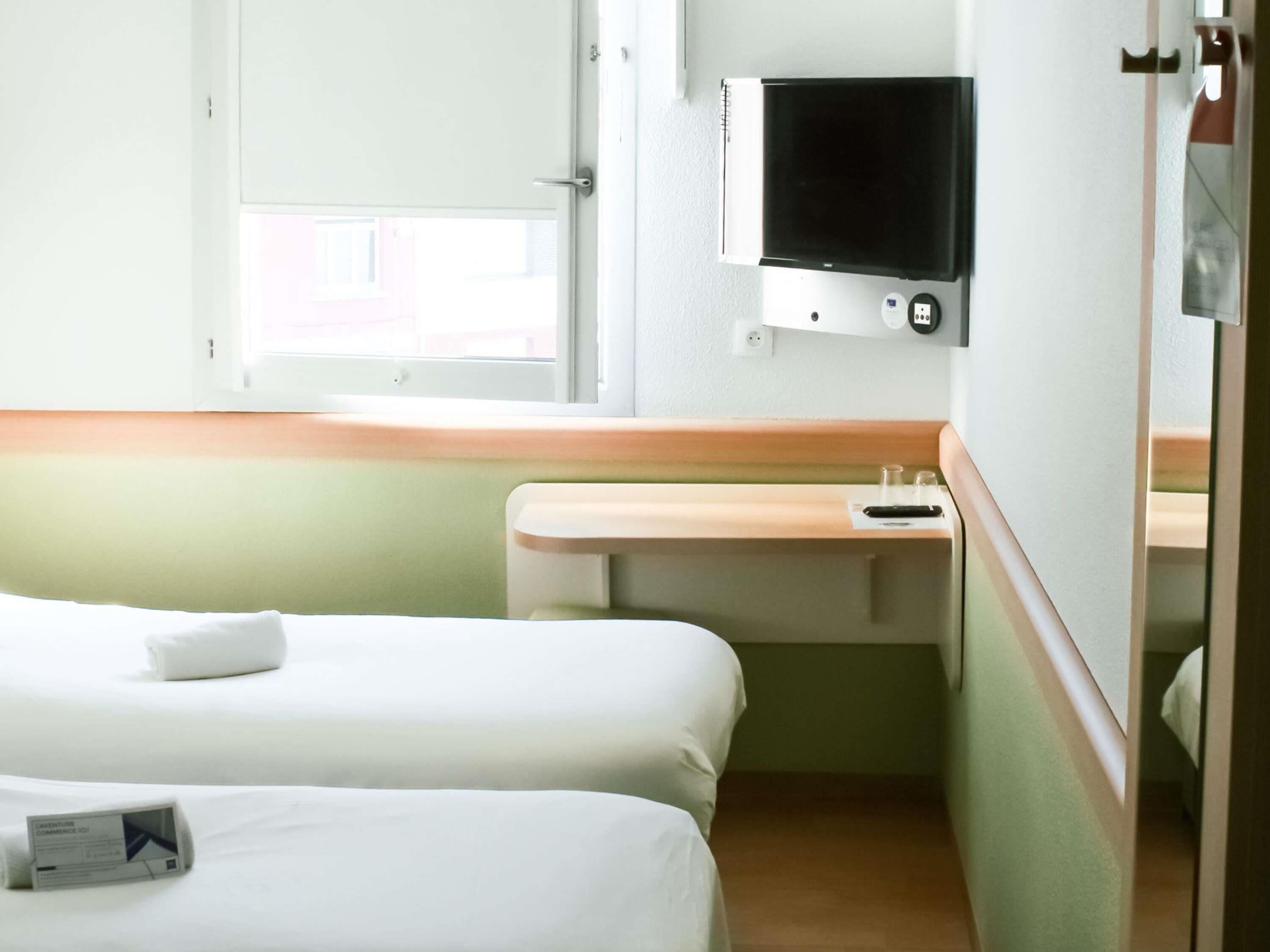 Een hotelkamer met twee bedden, een klein bureau met een televisie en een raam.