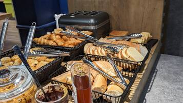 A buffet with various food items, including pastries, bread, and condiments.