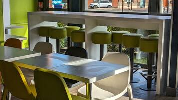 Un'area pranzo moderna con un tavolo grande e sedie, ampie finestre che offrono vista su edifici e un'auto all'esterno.