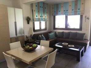 Un salon moderne avec un canapé, une table basse et une table à manger. Il y a une fenêtre avec des rideaux et une vue sur l’extérieur.