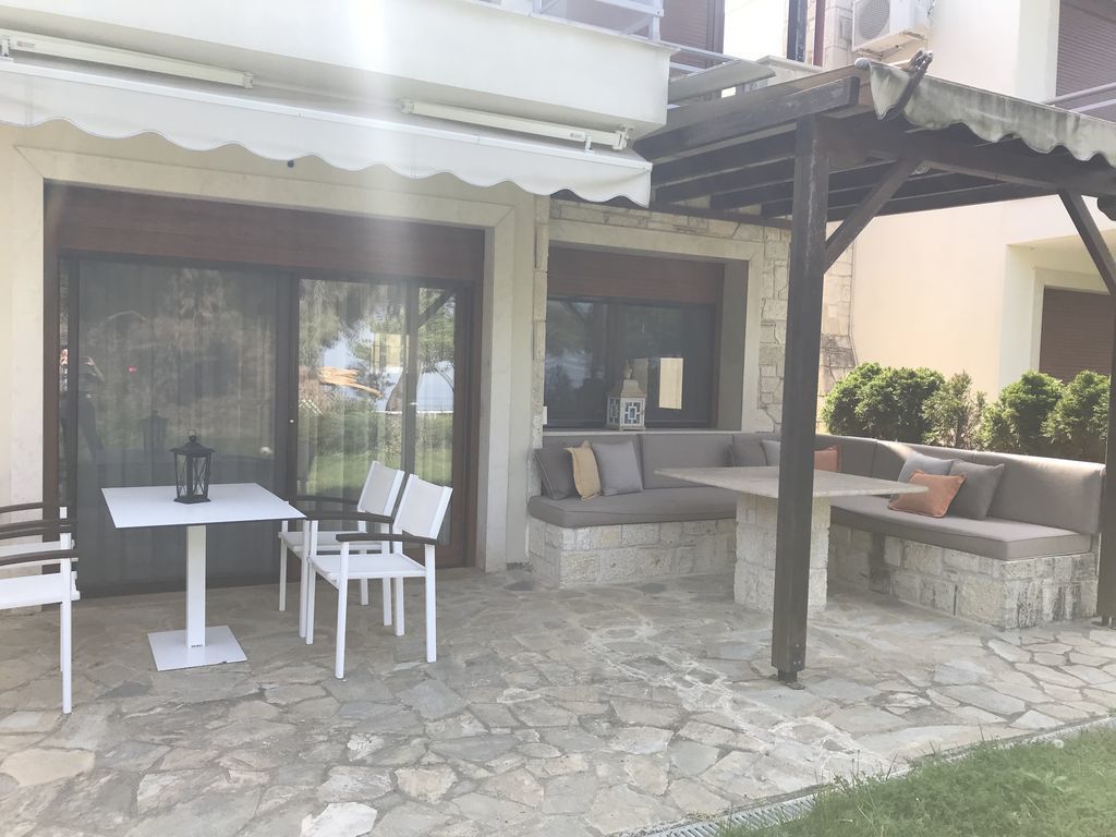An outdoor patio area with a stone floor, white furniture, and a covered seating area.