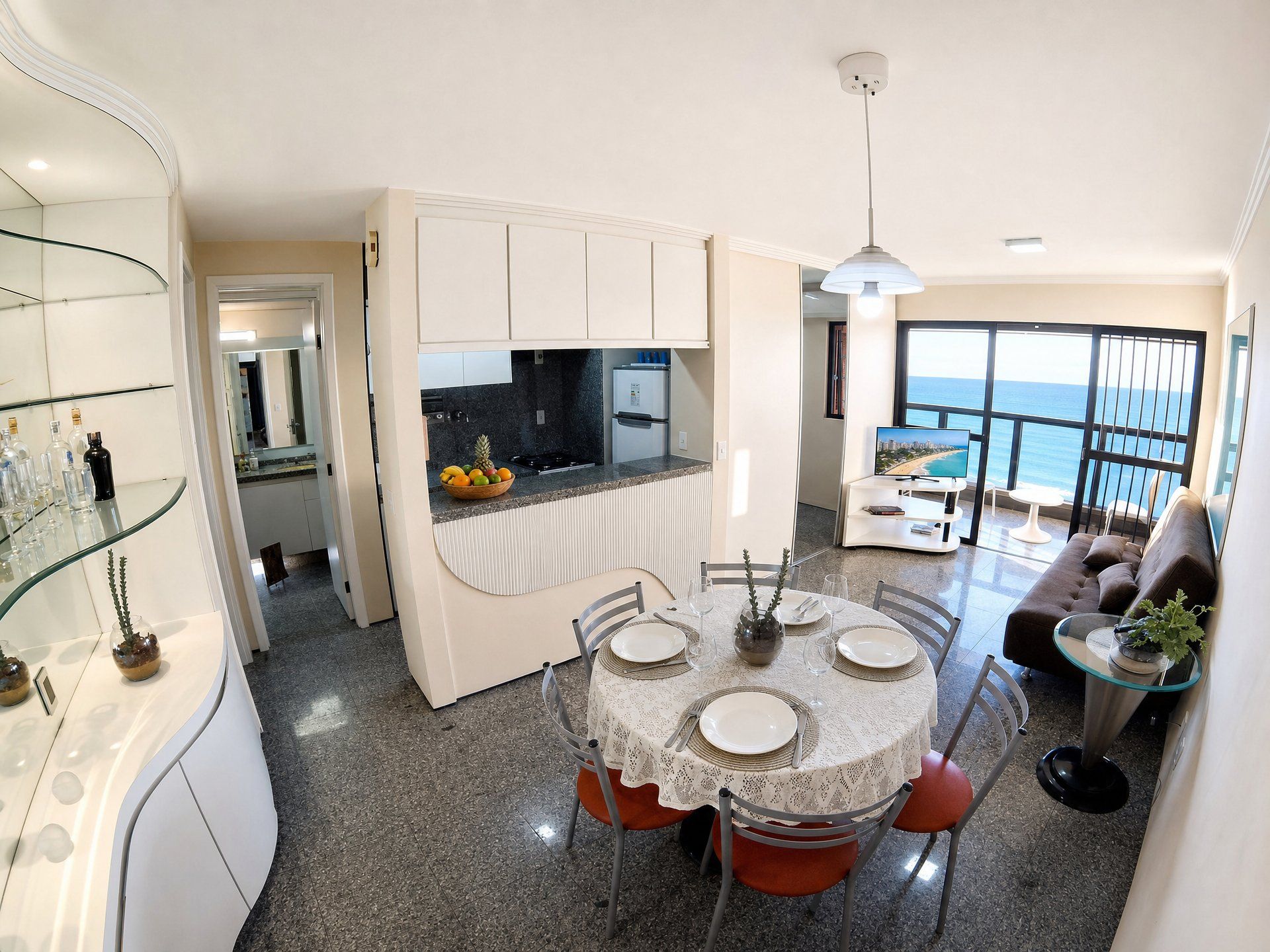 A modern kitchen with a dining area, a balcony with a view, and a living room with a sofa and a coffee table.