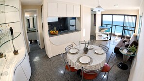 Cozinha moderna com área de refeições, varanda com vista e sala de estar com sofá e mesa de centro.