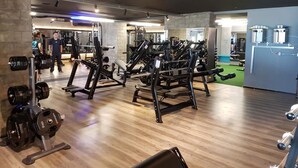 Een sportschool met diverse fitnessapparaten, waaronder loopbanden, krachtapparaten en losse gewichten.