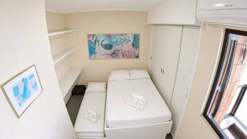 Quarto de hotel pequeno com cama, guarda-roupa, um quadro na parede e uma janela.