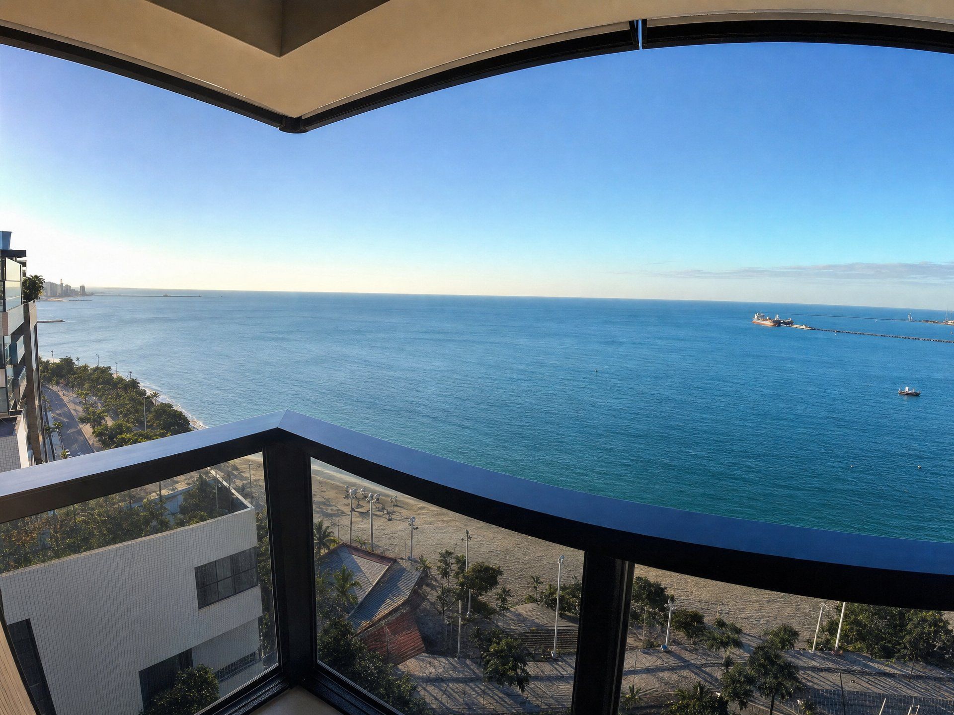 A balcony with a view of the sea, a distant city skyline, and a clear sky.