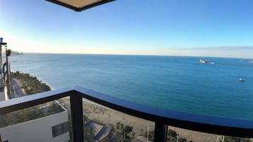 Un balcón con vista al mar, un horizonte lejano de la ciudad y un cielo despejado.