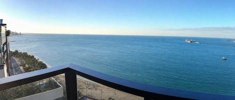 A balcony with a view of the sea, a distant city skyline, and a clear sky.