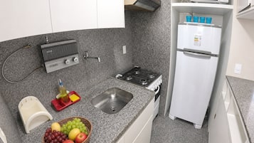 Cocina compacta con estufa a gas, lavamanos y refrigerador blanco.