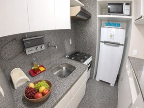 Cocina compacta con estufa a gas, lavamanos y refrigerador blanco.