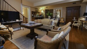 A cozy living room with a television, a coffee table, wicker furniture, and a staircase.