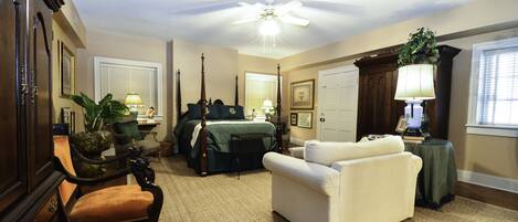 A well-lit bedroom with a four-poster bed, a ceiling fan, and a large window.