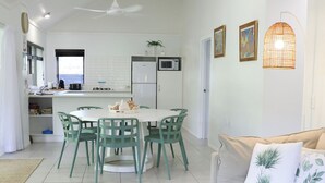 A modern kitchen with white cabinets, a dining area with green chairs, and a ceiling fan. - Makayla Palms (Rarotonga)