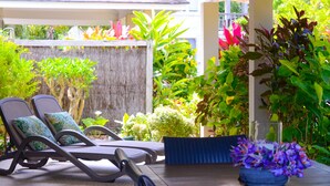 A patio with two lounge chairs, a table with a vase of flowers, and lush greenery. - Makayla Palms (Rarotonga)