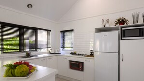 A modern kitchen with white cabinets, a built-in oven, a microwave, and a refrigerator. - Makayla Palms (Rarotonga)