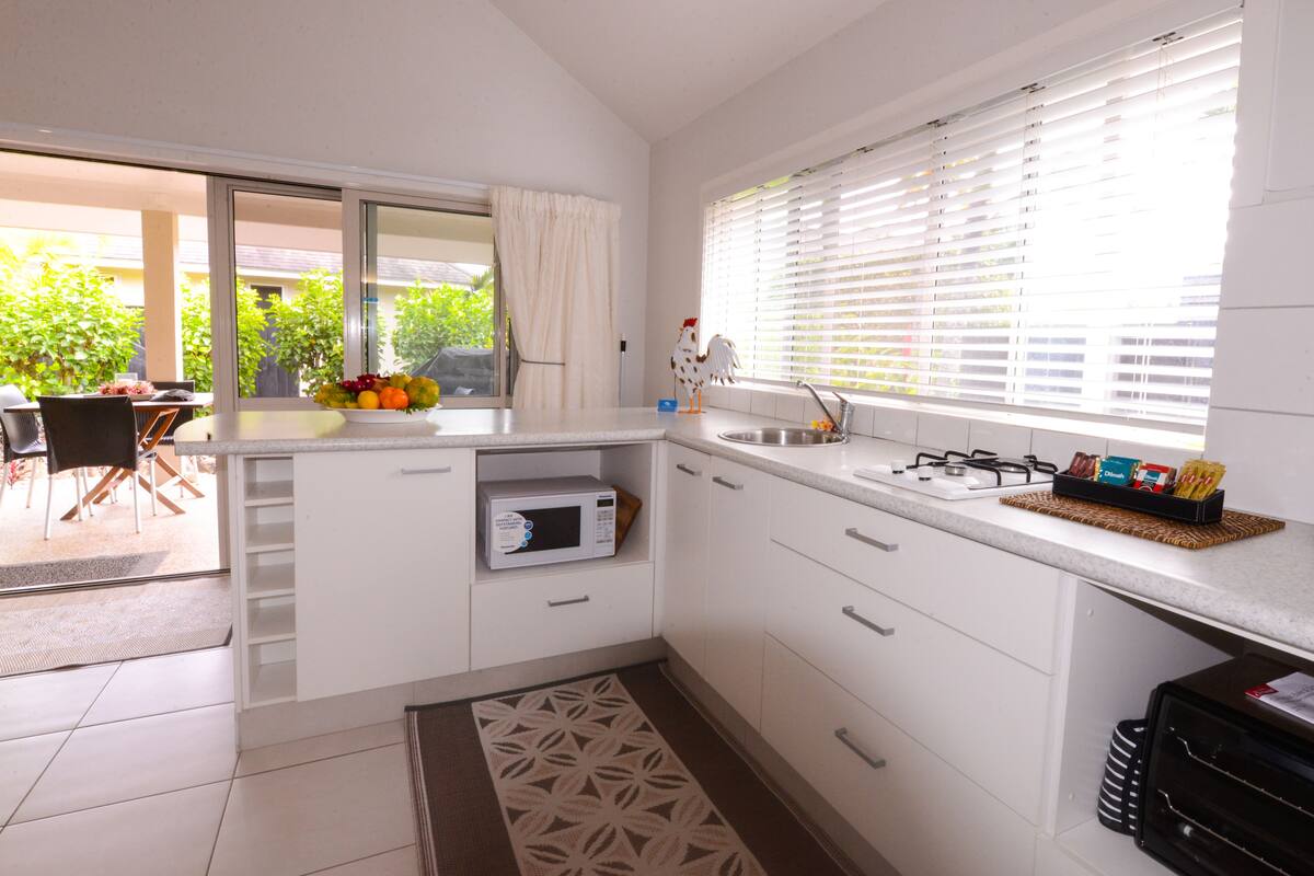 A modern kitchen with white cabinets, a built-in microwave, a sink, and a window with blinds.