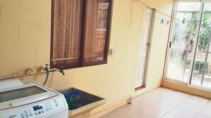 Zona de lavandería con lavadora, un lavamanos pequeño y una ventana con cortinas.