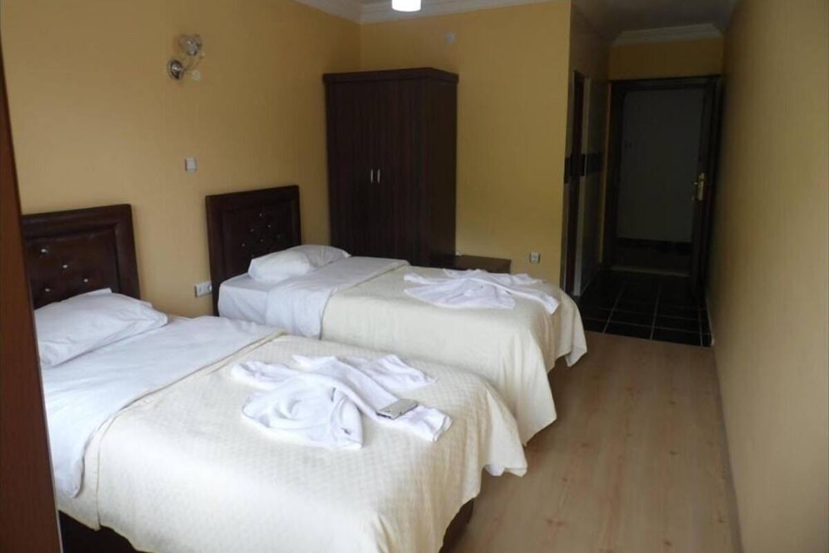 A hotel room with two beds, wooden headboards, a wardrobe, and a door leading to another room.