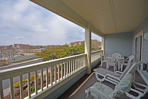 A balcony with a view of a residential area, outdoor furniture, and a covered section with a table and chairs.