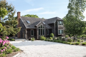 A two-story house with a brick chimney, large windows, and a gravel driveway.